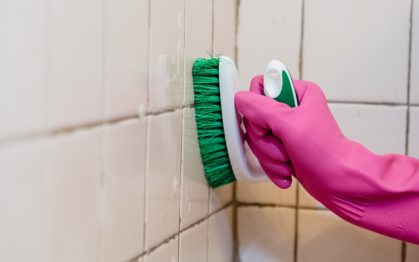 Gloved hand scrubbing tile grout with a brush during a deep clean