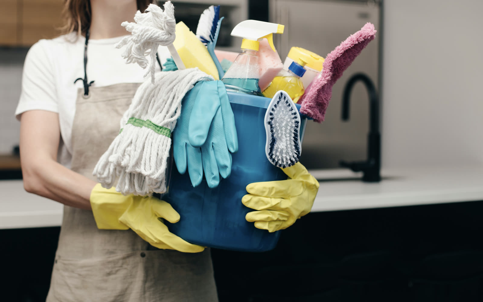 Cleaner carrying a bucket of cleaning supplies into a kitchen